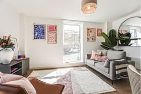 A living room with a grey couch, a brown chair, a white vase with flowers, a rug, and pictures on the wall.