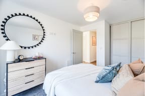 A bedroom with a white bed and a black dresser with a round mirror above it.