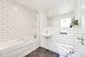 A white tiled bathroom with a toilet, sink, and bathtub.