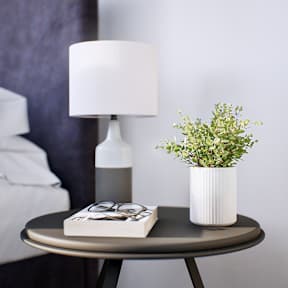 A table with a lamp, a book, glasses, and a plant on it.