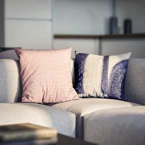 A grey couch with a pink and a blue and white pillow on it.