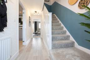 A long hallway with a staircase and a mirror on the wall.