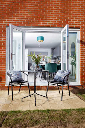 A table with two chairs is outside a house.