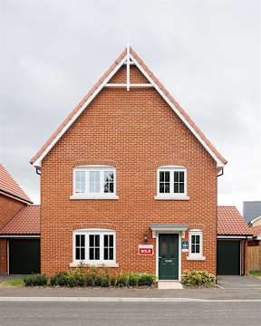 A red brick house with a green door and a "Sold" sign in the window.
