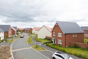 A residential street with houses on both sides and cars parked on the side of the road.