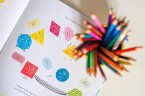 A book with colorful shapes and a bunch of colored pencils.
