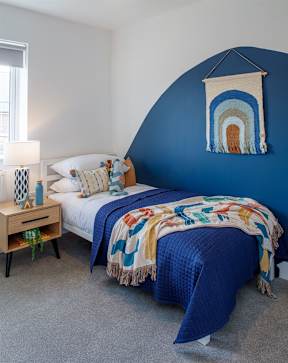 A bedroom with a blue bed and a wall hanging.