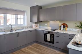 A modern kitchen with grey cabinets and a wooden floor.