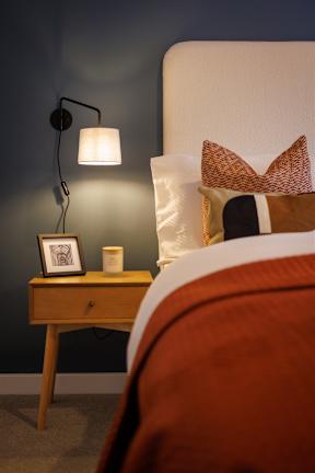 A bedroom with a bed, a nightstand with a lamp and a picture frame on it.