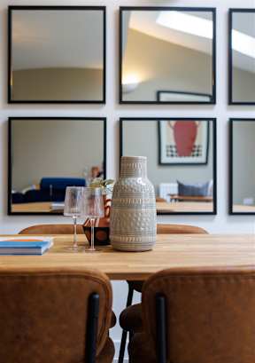 A table with a bottle and glasses on it with a book and a chair.
