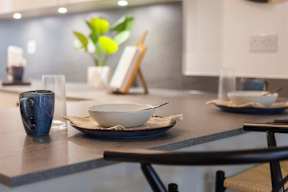 A blue mug sits on a table with a bowl and a vase of flowers.