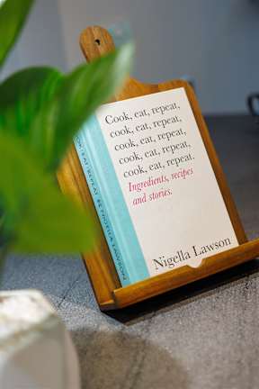 A book titled "Cook, eat, repeat" by Nigella Lawson is displayed on a wooden stand.
