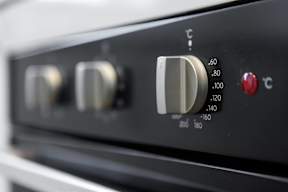 A close up of a black oven control panel with three knobs and a red button.