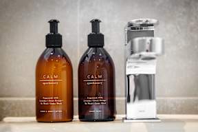 Two bottles of Calm hand soap and a soap dispenser on a bathroom counter.
