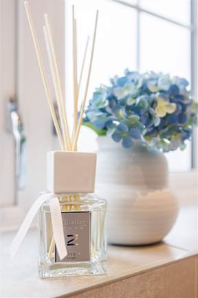A bottle of Z Estee Lauder perfume sits on a table next to a vase of flowers.