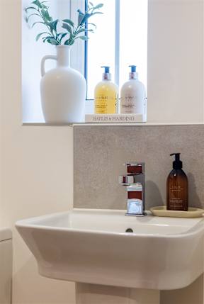 A white sink with a tray holding a bottle of body wash and a bottle of lotion.