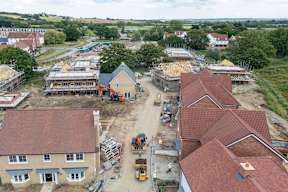 A construction site with a building under construction and a red roofed building in the foreground.