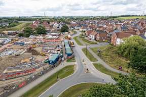 A construction site is seen in the foreground of a residential area.