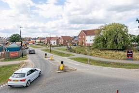 A car is driving on a road with a yellow box junction ahead.
