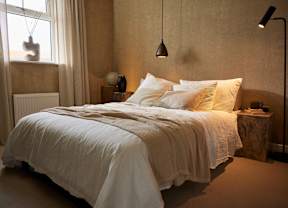 A bed with white bedding sits in a room with a window.