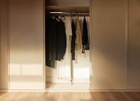 Clothes hanging in a closet with light coming through the door.