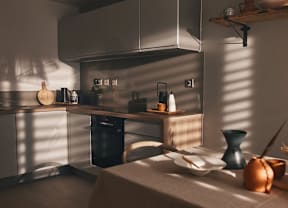 A kitchen with a black dishwasher and a wooden cutting board on the counter.