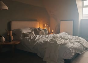 A bed with white sheets and pillows is in a room with a lamp on a side table.