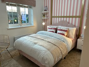 A bedroom with a bed, chair, and striped wallpaper.