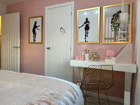 A bedroom with a bed, desk, chair, and two framed silhouettes on the wall.