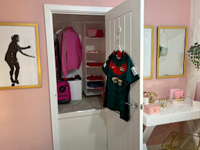 A white closet with a pink suitcase and a green shirt hanging on it.
