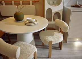 A white round table with a green vase and a white chair with a textured seat.