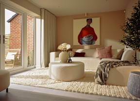 A living room with a white couch, a round ottoman, and a painting of a woman on the wall.