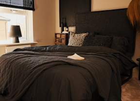 A bed with a black comforter and a white pillow on it.