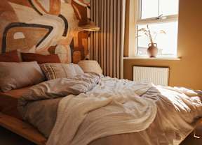 A bed with a white blanket and pillows in front of a wall with a large abstract painting.