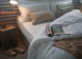 A bed with a book and slippers on the side table.