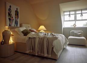 A bedroom with a bed, a lamp, and a painting on the wall.