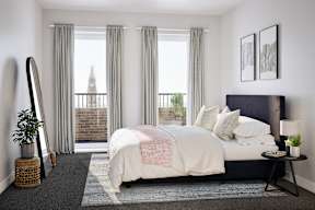 A bedroom with a large bed and a view of a building outside the window.