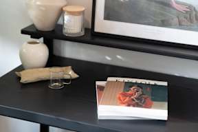 A black table with a glass, a book, and a vase on it.