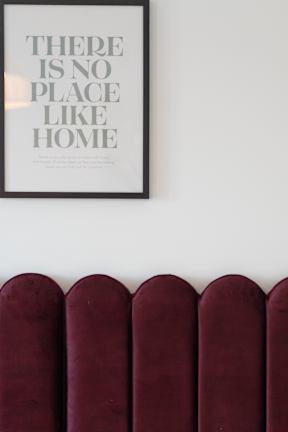 A poster with the text "There is no place like home" hangs on a wall above a row of burgundy headboards.