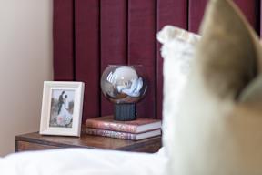 A bedroom with a white pillow and a nightstand with a picture frame and books.