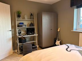 A room with a bed, a shelf with electronics, and a guitar.