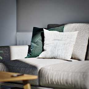 A grey couch with a green and white pillow on it.