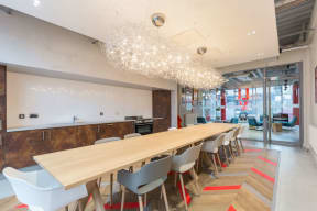 a long communal table with chairs in a room with a kitchen