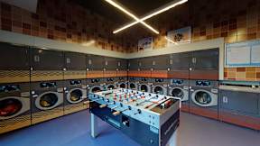 A foosball table is in the middle of a room with washing machines on the wall.