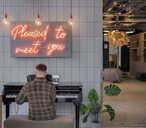 A man is sitting at a piano in a room with a neon sign that says "Pleased to meet you."