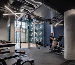 A man is working out on a stationary bike in a gym with a concrete column and a row of treadmills.