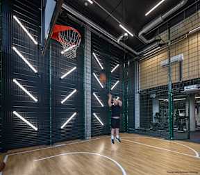 A man is playing basketball in a gym with a basketball hoop and a wooden floor.