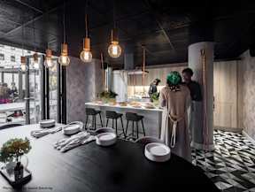 A modern dining area with a black table and chairs, and people standing in the background.