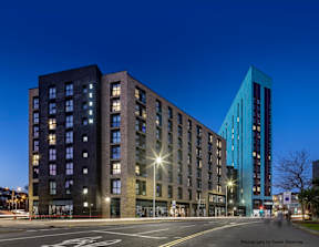 A modern building with a glass facade stands next to a traditional brick building at dusk.