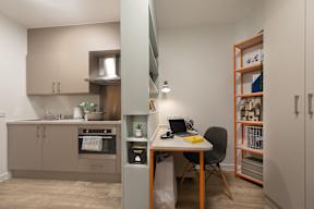 A small kitchen with a desk and chair in the middle.